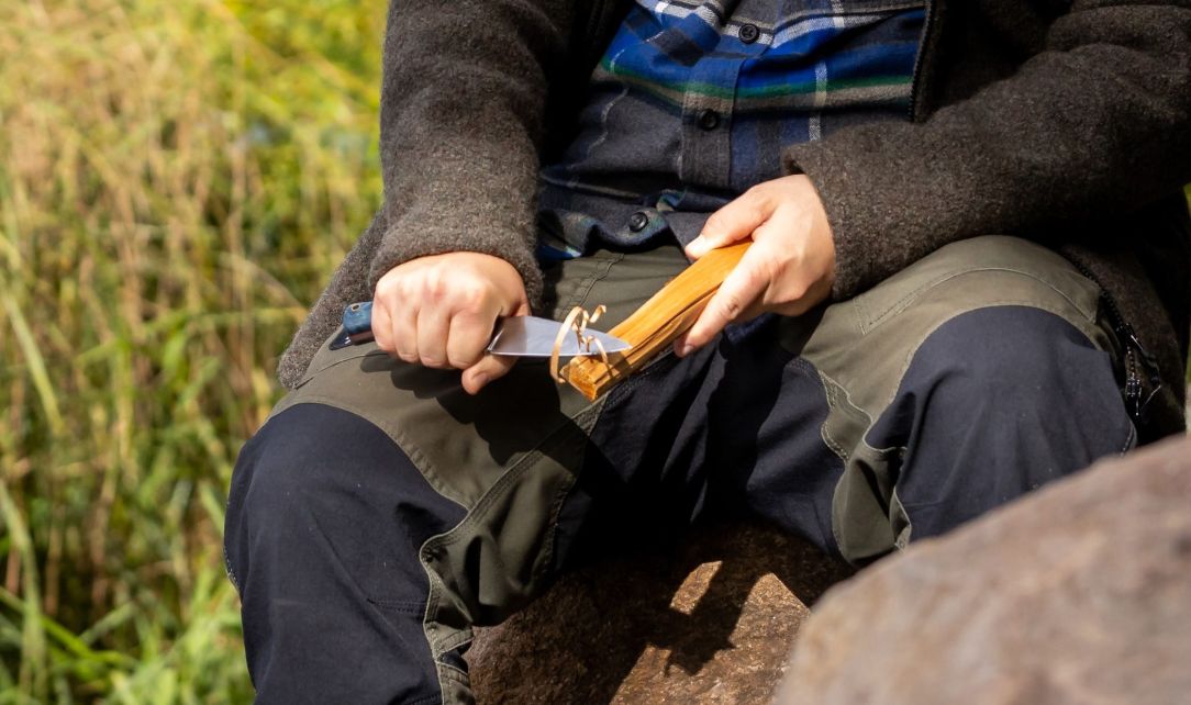 Person schnitzt mit Messer ein Stück Holz