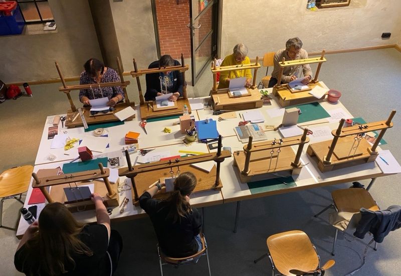 Personen sitzen am Tisch und binden Bücher